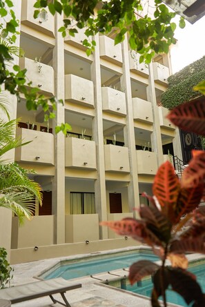 Un edificio de varios pisos con balcones, piscina y vegetación circundante.