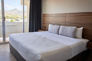 Habitación de hotel con una cama grande, cabecera de madera y vistas a la montaña a través de una puerta corrediza.
