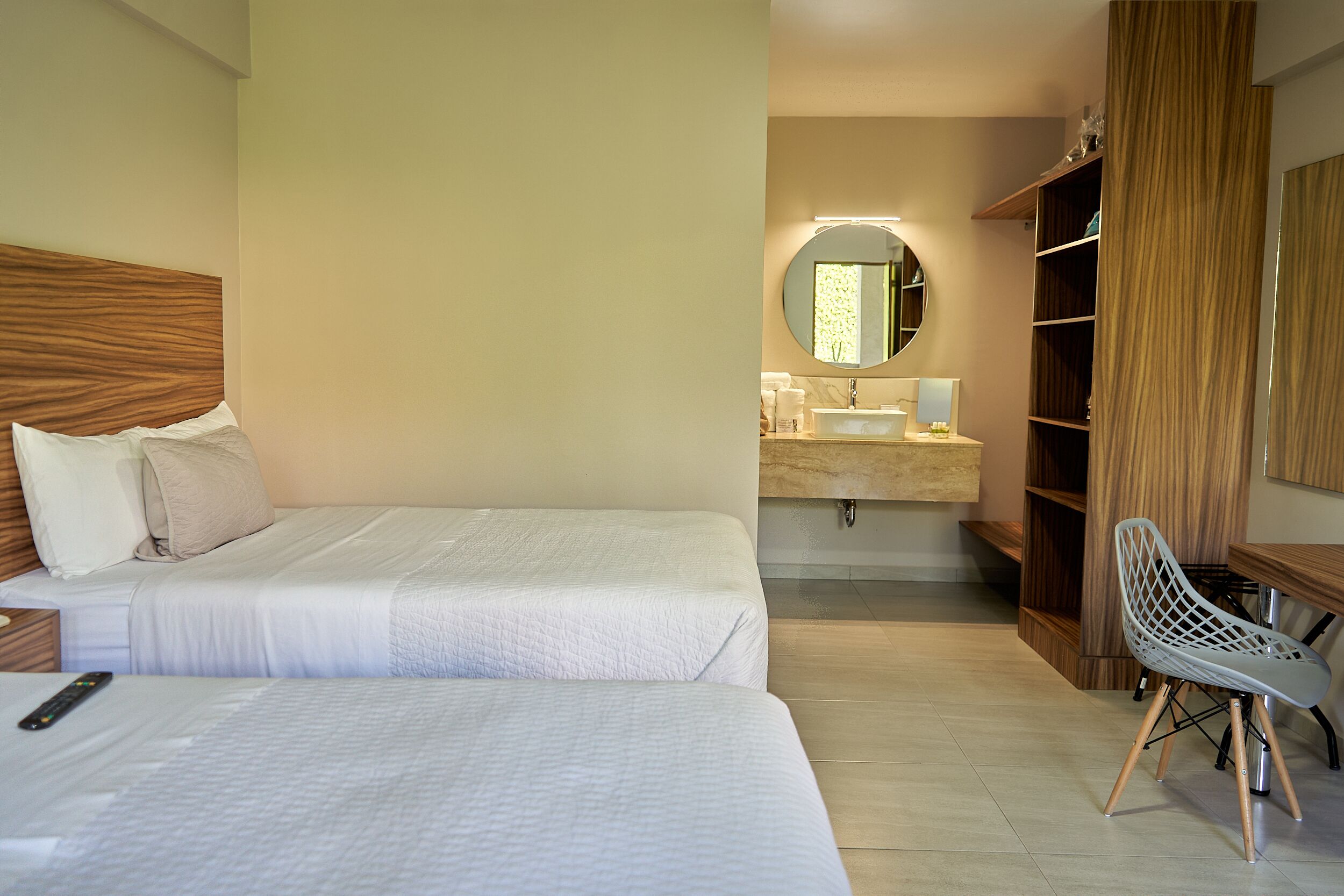 A hotel room with two beds, a bathroom with a sink and mirror, and a wooden wardrobe.