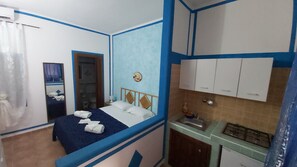 A compact hotel room with a bed, a small kitchenette, and a bathroom.