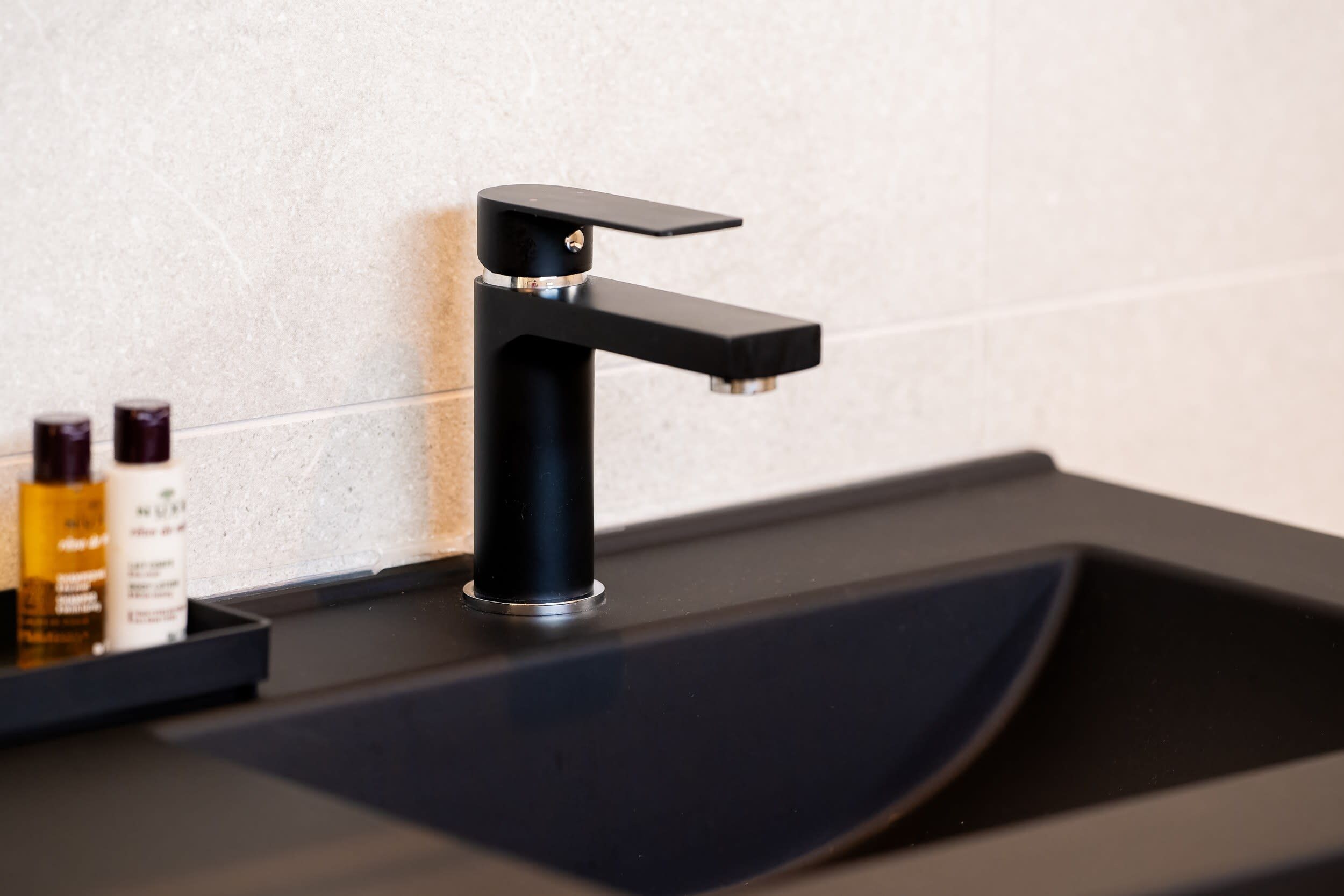 Un robinet noir fixé sur un lavabo noir, avec un mur recouvert de carreaux blancs en arrière-plan.