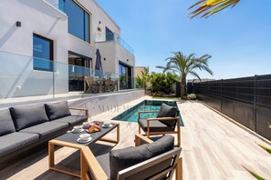 Un espace piscine extérieur moderne, comprenant un canapé et des fauteuils, une table à manger et une balustrade en verre.