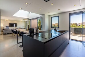 A modern kitchen with a large island, a dining area with a sofa and chairs, and a view of the outside through a glass door. - Villa Monégasque, elegance & exclusive seaside getaway (Sérignan)