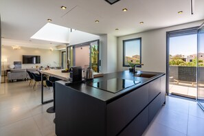A modern kitchen with a large island, a dining area with a sofa and chairs, and a TV mounted on the wall. - Villa Monégasque, elegance & exclusive seaside getaway (Sérignan)