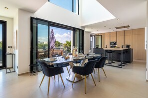 Une cuisine moderne dotée d’un îlot central, d’un coin repas avec une table en verre et d’une vue sur l’extérieur.