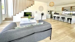 A modern living room with a grey sofa, a staircase, a kitchen area, and a dining space. - Into The Sea - 5 mins from the Beach (Albion)