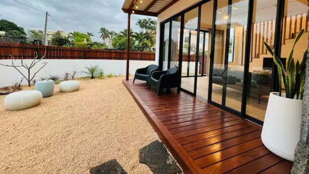 A modern outdoor patio with a wooden deck, seating area, and large glass doors leading to a living space. - Into The Sea - 5 mins from the Beach (Albion)