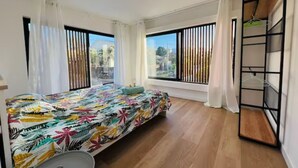 A bedroom with a bed, a window, a metal shelf unit, and a view of the outdoors. - Into The Sea - 5 mins from the Beach (Albion)