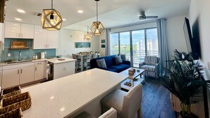 Una cocina moderna con una isla central, luces colgantes y una zona de comedor con sofá y sillas azules.