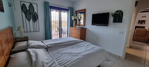 Une chambre avec un lit, une commode, un téléviseur et une porte coulissante donnant sur un balcon.