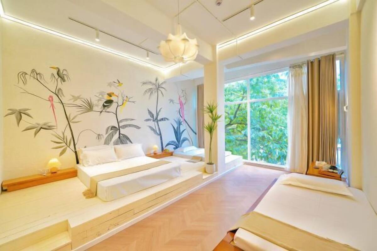 Una habitación de hotel moderna con un ventanal grande, una cama, un sofá y un mural en la pared.