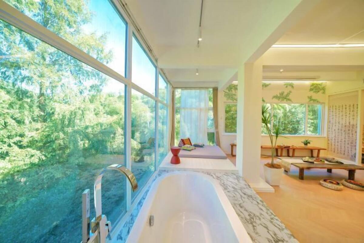 Un baño moderno con una bañera grande, una zona de ducha y un área de descanso con vistas al bosque.