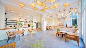 Un amplio hall de hotel con zona de comedor central, diversas opciones de asientos y una cocina visible al fondo.
