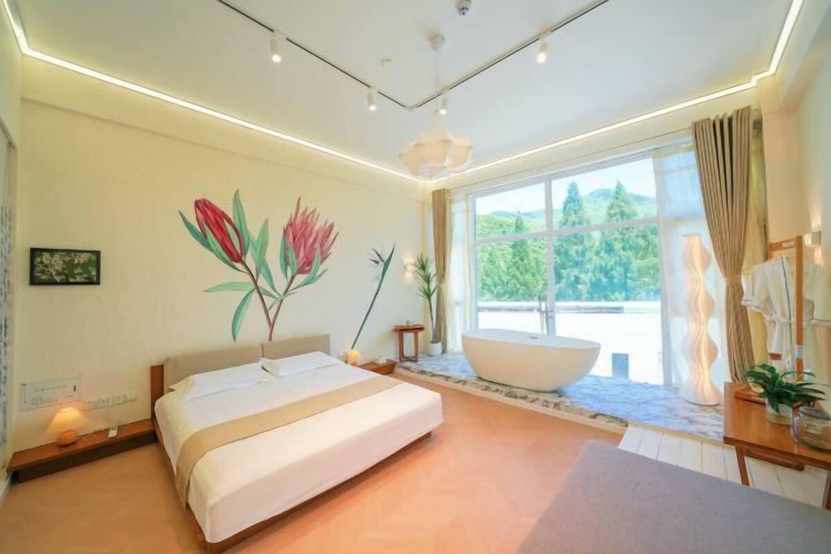 Un dormitorio moderno con una cama grande, una bañera y vistas a zonas verdes.