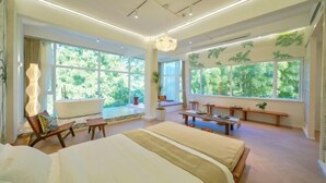Un dormitorio espacioso con una cama grande, varios rincones de descanso y amplias ventanas con vistas a zonas verdes.