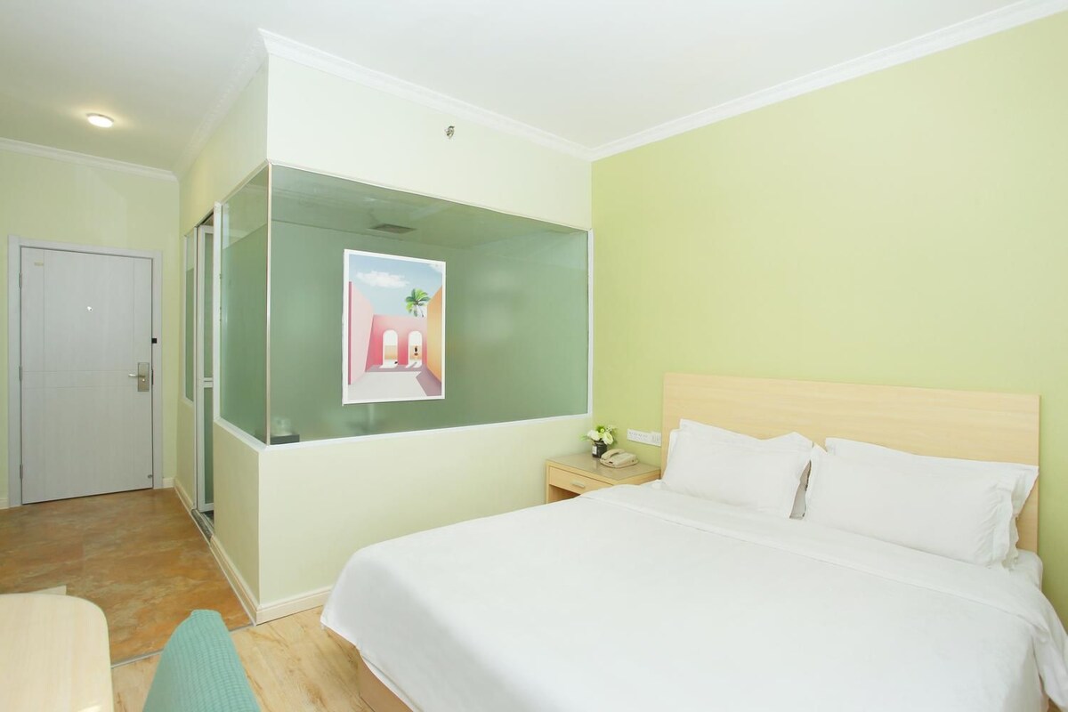 A hotel room with a bed, a nightstand, a wall-mounted artwork, and a door.