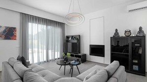 Un salon moderne avec un canapé gris, une petite table ronde, un téléviseur et une cheminée.