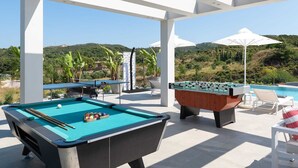 Un espace extérieur avec une piscine, une table de baby-foot, une table de billard et des chaises longues.