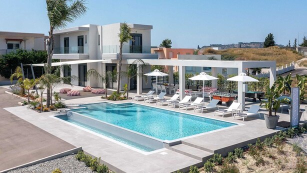 Un espace piscine moderne avec des chaises longues, des parasols et une piscine à l’eau d’un bleu limpide.