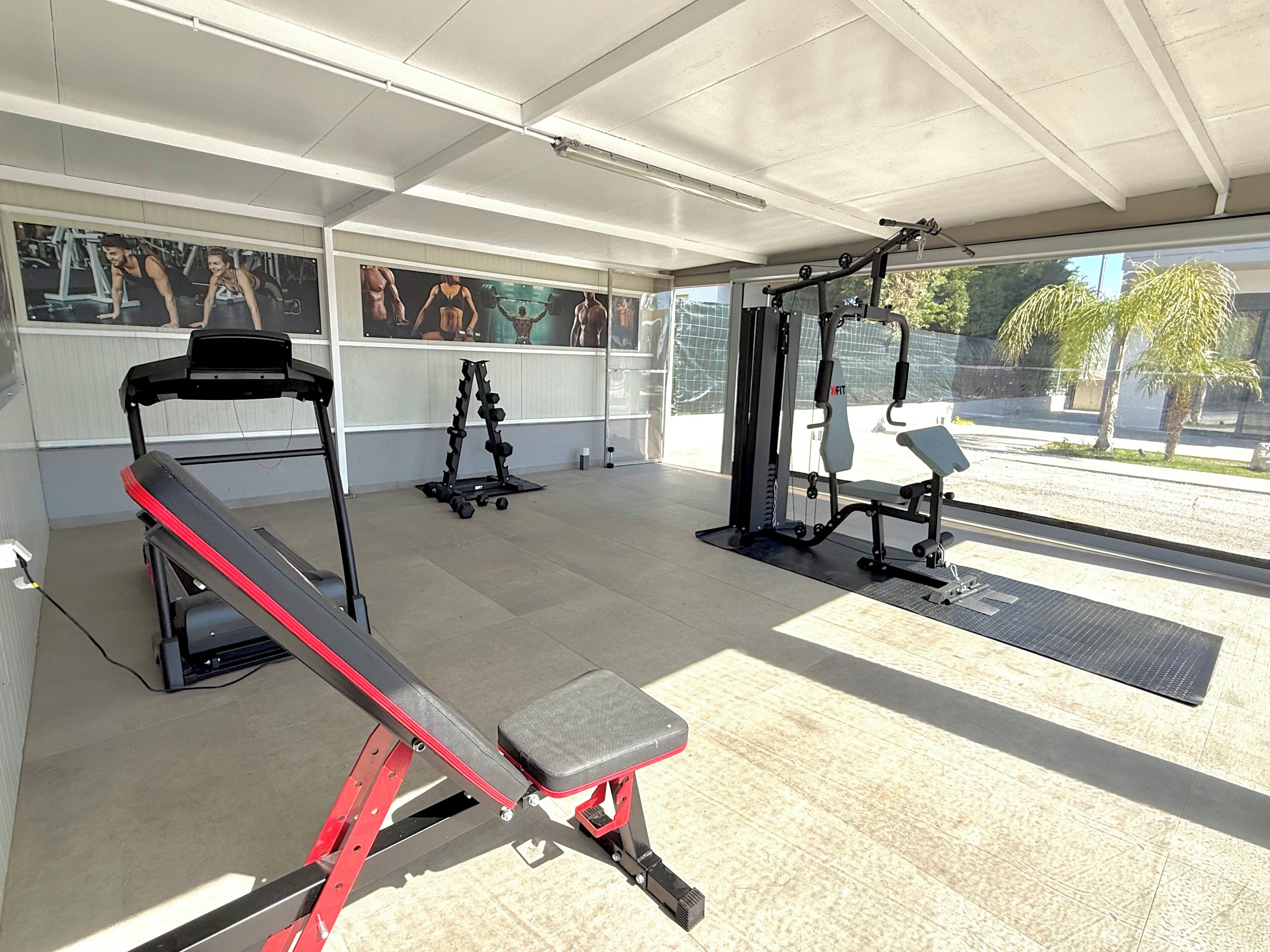 A gym with exercise equipment, a bench, and a wall with fitness posters.