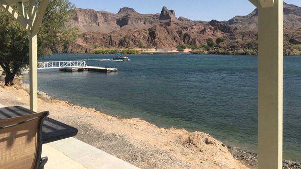 A riverside view with a wooden pier, a boat, and rocky mountains in the background. - Margaritaville at River Lodge! Right on the river! (Parker Dam)