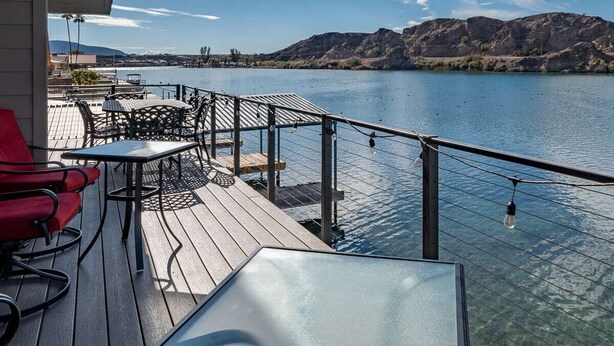 A deck with outdoor seating, overlooking a body of water and distant hills.