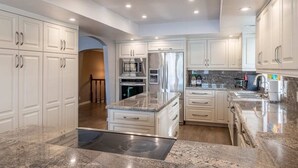 A modern kitchen with white cabinetry, stainless steel appliances, granite countertops, and recessed ceiling lighting.