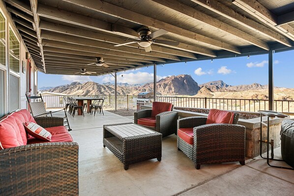 Patio esterno con mobili in vimini, una ventola a soffitto e vista sulle montagne.