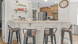 A kitchen with a central island, bar stools, wooden cabinets, and pendant lighting. - Bayview Beauty! Private River access and mountain views! (Parker)