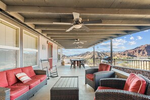 Portico esterno coperto con mobili in vimini, ventilatori a soffitto e vista sulle montagne.