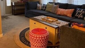 Una sala de estar con un sofá, un reposapiés y un televisor en la pared.