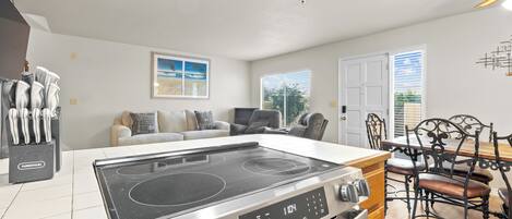 A modern kitchen with a built-in stove, dining area with chairs, and a sofa.