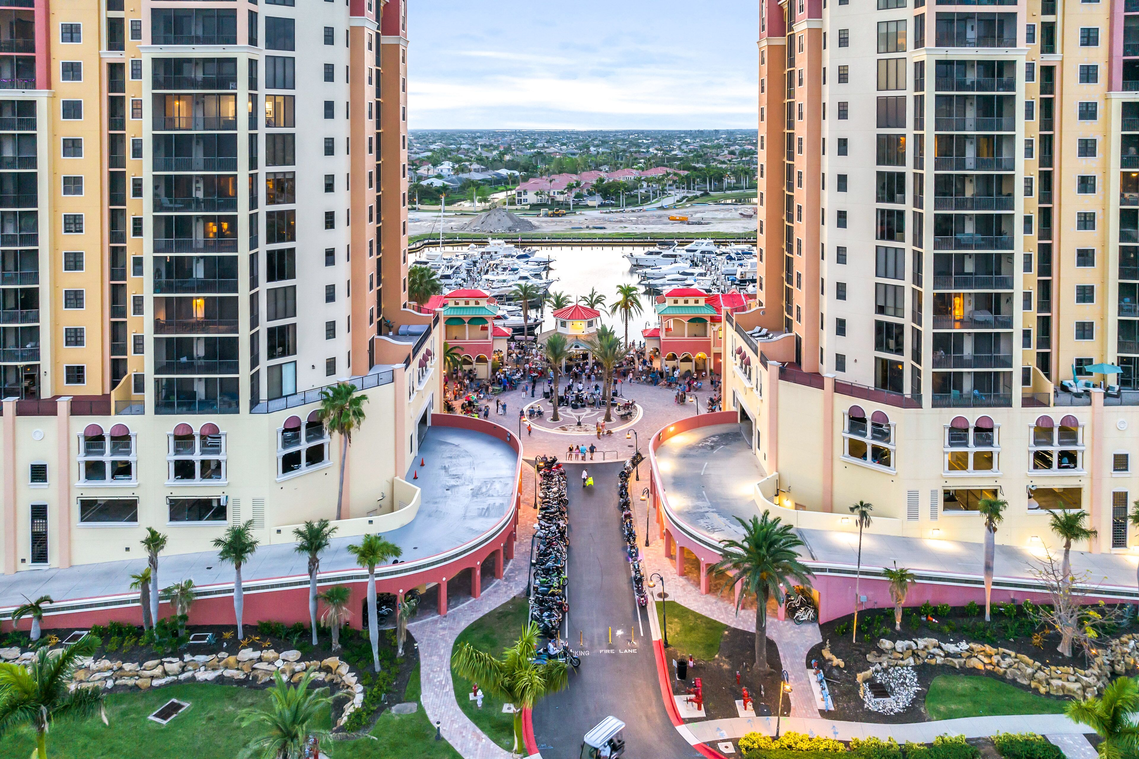 A high-rise hotel with a central courtyard, multiple balconies, and a marina in the background.