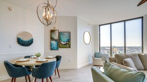 A modern dining area with a round table, blue chairs, and a chandelier. - Condo w/ Views & Resort Amenities in Cape Harbour! (Cape Coral)