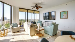 A modern living room with large windows, a ceiling fan, and a flat-screen TV. - Condo w/ Views & Resort Amenities in Cape Harbour! (Cape Coral)