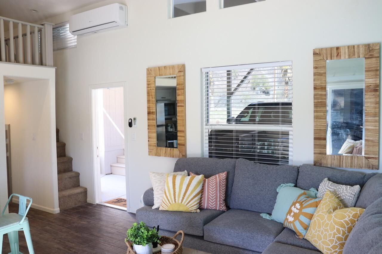 A modern living room with a grey sofa, decorative pillows, a coffee table with a plant, and a staircase leading to an upper level.