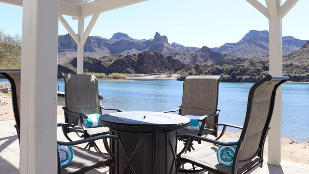 A covered patio with two chairs and a table, overlooking a lake and mountains.