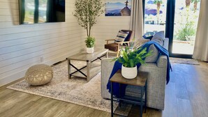 A cozy living room with a sofa, a coffee table, and a chair. There is a large window with a view of palm trees and mountains. - Castle Rock 95, 4brs, Community launch, Riverfront park (Parker)