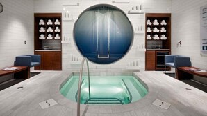 A modern spa with a central circular pool, wooden benches, and shelves with white decorative items. - Gorgeous Suites Vdara (Las Vegas)