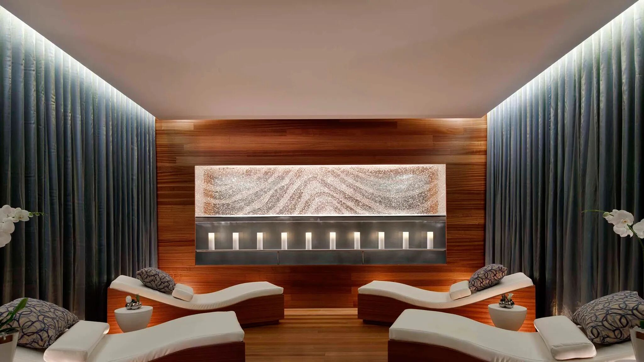 Een moderne spa-ruimte met twee relaxbestendige stoelen, een groot wandpaneel met verlichting en verticale houten panelen.