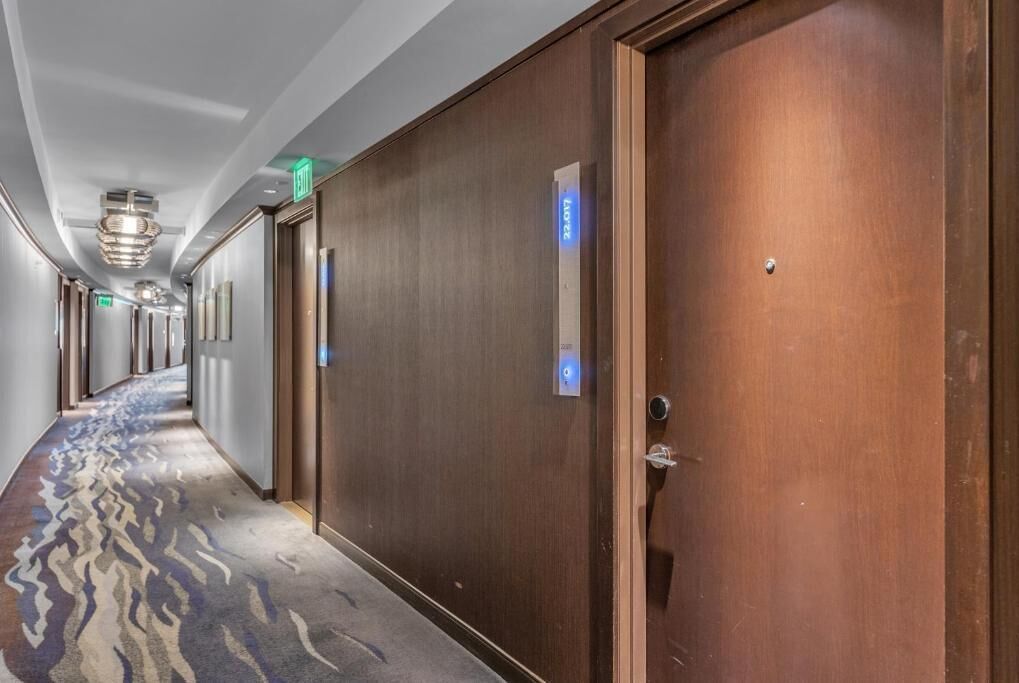 A hotel hallway with wooden doors, a patterned carpet, and a modern light fixture.