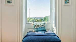 A bedroom with a large window, a bed with a blue blanket, and a pillow with the word "BEACH" on it.