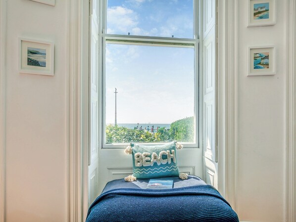 A bedroom with a large window, a bed with a blue blanket, and a pillow with the word "BEACH" on it.