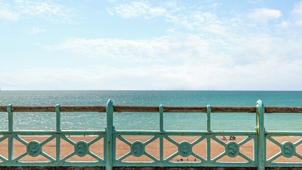 A beach with a turquoise railing and a clear sky.