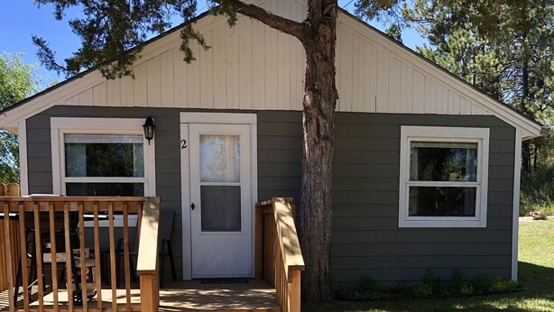 A small, single-story building with a porch and a door, surrounded by gravel and trees. - Cabin by lake, pet friendly, quiet (Hot Springs)
