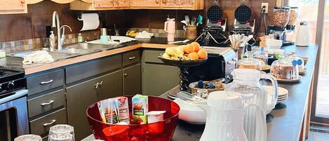 A kitchen with wooden cabinets, a large island with various food items, a waffle maker, and a coffee machine.