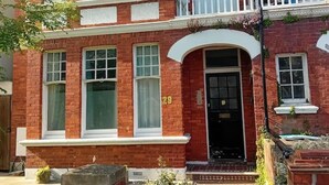 A two-story red brick building with a black front door, white windows, and a small balcony. - Modern Spacious Apartment Families & Corporate (Hove)