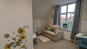 A cozy living room with a beige sofa, a small side table, and a window with curtains. - Modern Spacious Apartment Families & Corporate (Hove)
