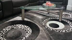 Uma sala de estar moderna com um sofá em couro preto, almofadas vermelhas, uma mesa de centro de vidro e um tapete estampado.