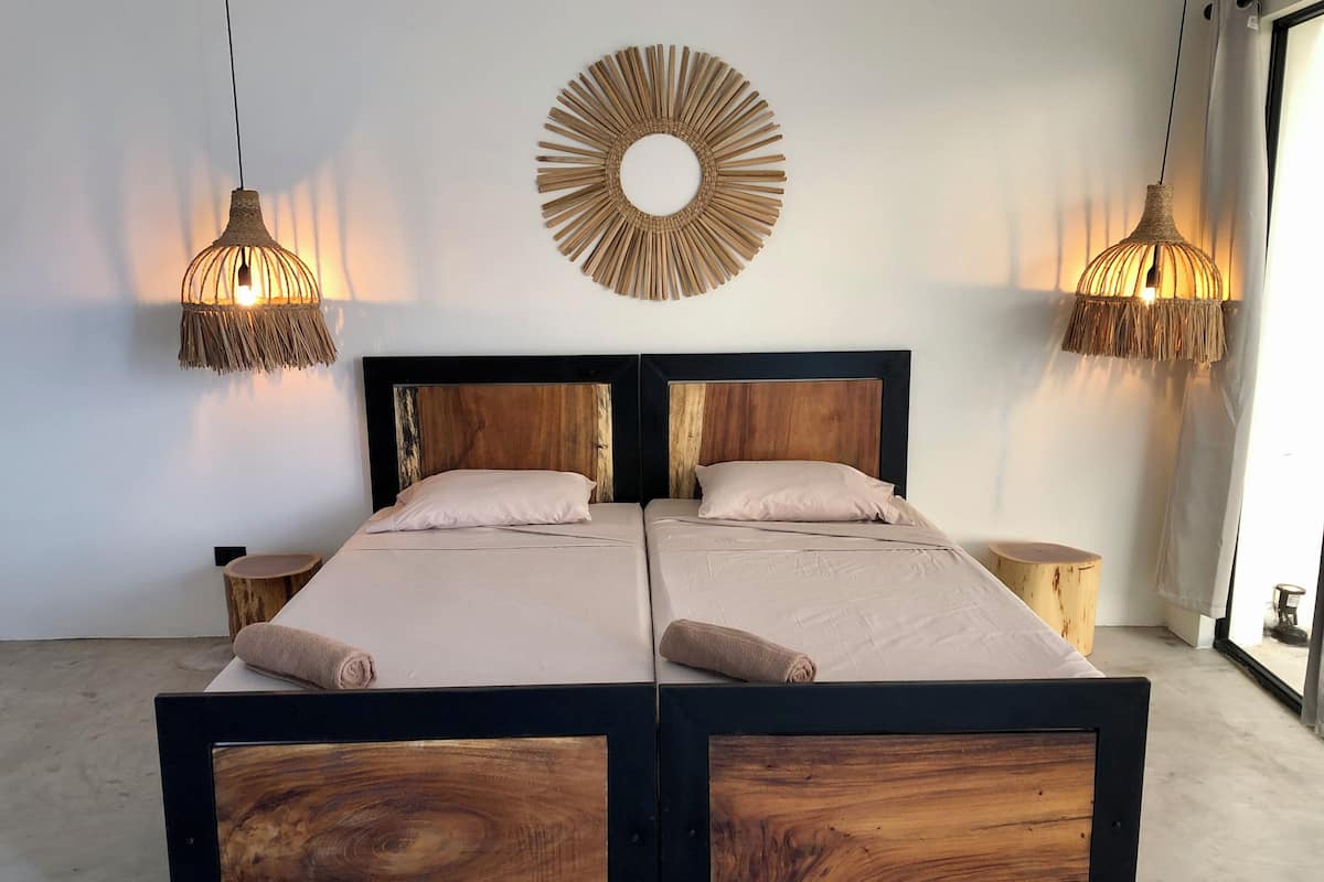 A double bed with a wooden frame and headboard, two bedside tables, a round wall decoration, and hanging lamps.